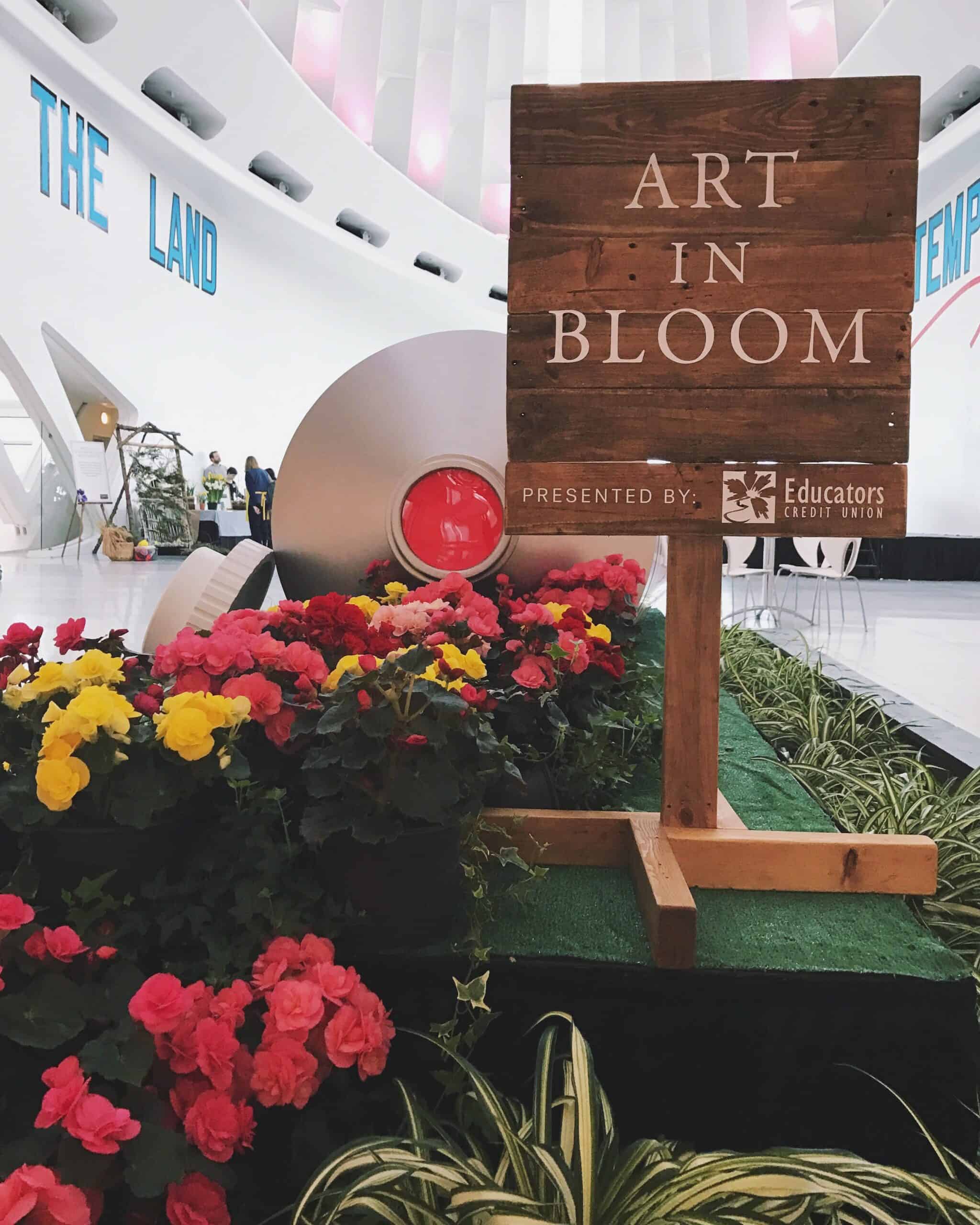 a sign with the words "art in bloom, presented by Educators Credit Union" amongst a display of flowers