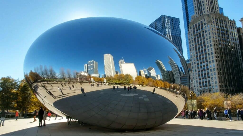 reflective oval shaped sculpture with people standing around and buildings in the background