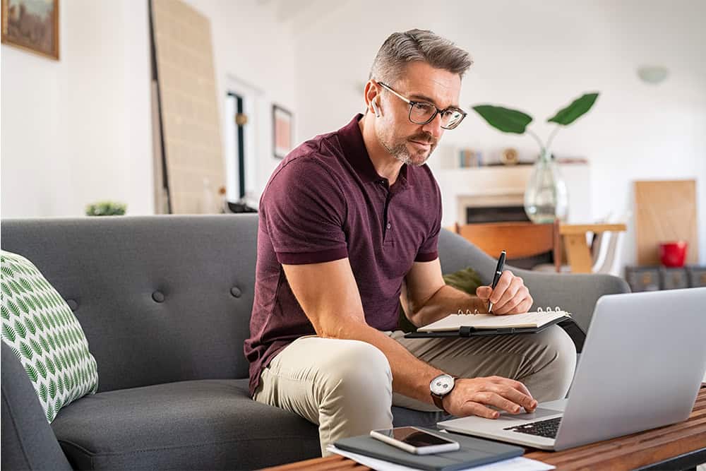 A man using laptop and notebook at home, to get preapproved for a loan.