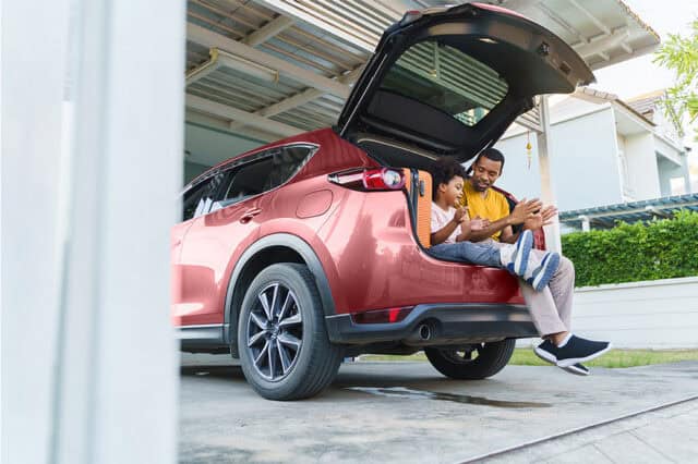 Family loading luggage into the trunk of a red SUV for a road trip.