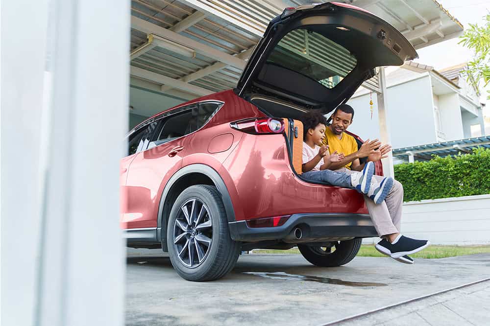 Family loading luggage into the trunk of a red SUV for a road trip.