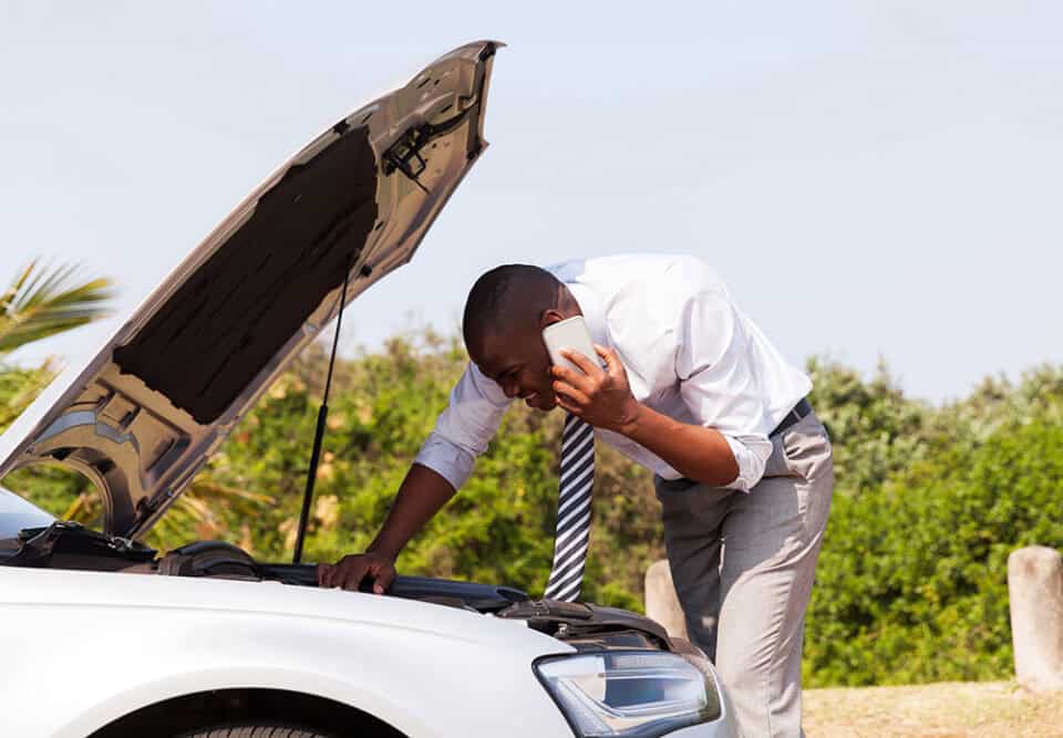 Man checking car engine while talking on phone outdoors, representing auto extended warranty support.