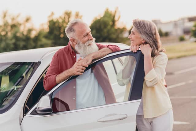 Elderly man and woman enjoying conversation outside a car, having found their dream car.