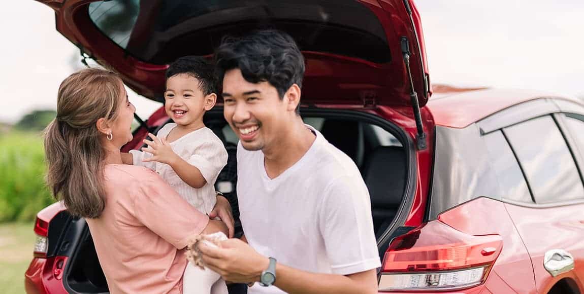 Happy family with child hanging out near the trunk of their new leased car.