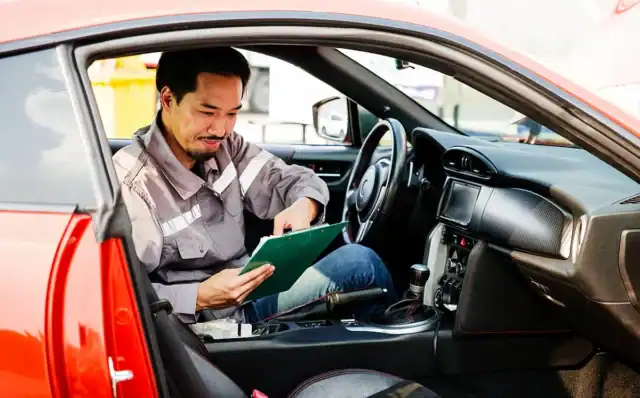 Auto trade-in technician reviewing data on tablet inside a vehicle for maintenance or diagnostics.