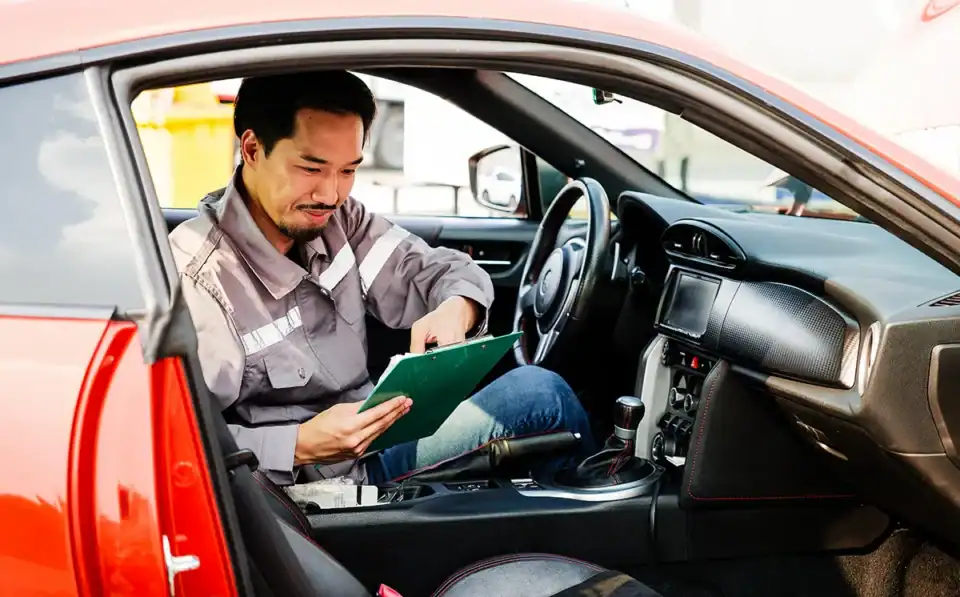 Auto trade-in technician reviewing data on tablet inside a vehicle for maintenance or diagnostics.