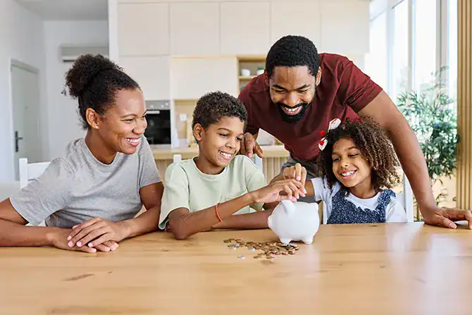 Parents saving coins in a piggy bank with kids as they discuss money management topics during back-to-school season.
