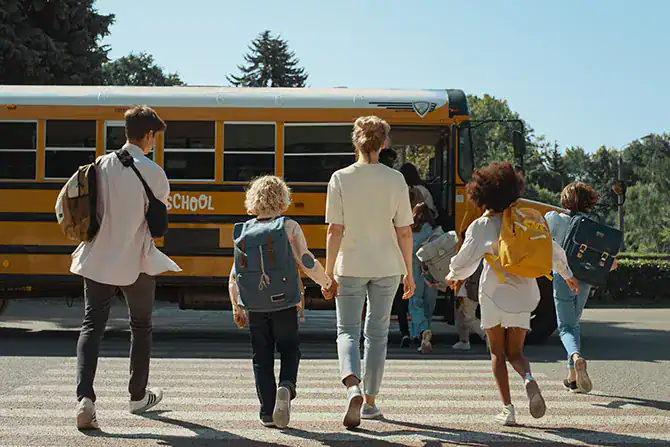 Children and a parent heading back to school by walking towards a school bus.