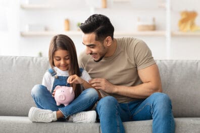 Papá e hija poniendo dinero en una alcancía