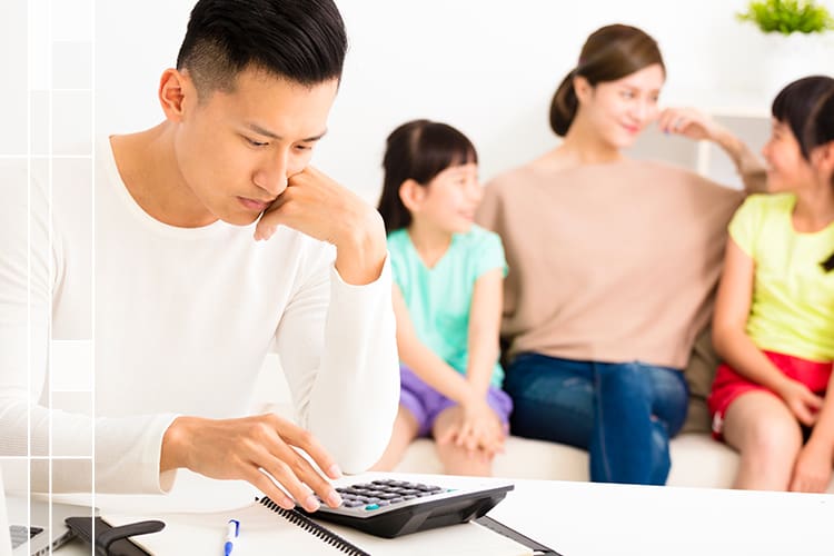 father working on bills with wife and kids behind him on a couch