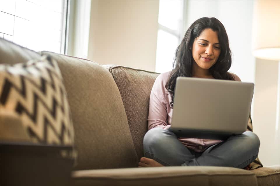Una mujer se sienta en un sofá mientras trabaja en su computadora portátil