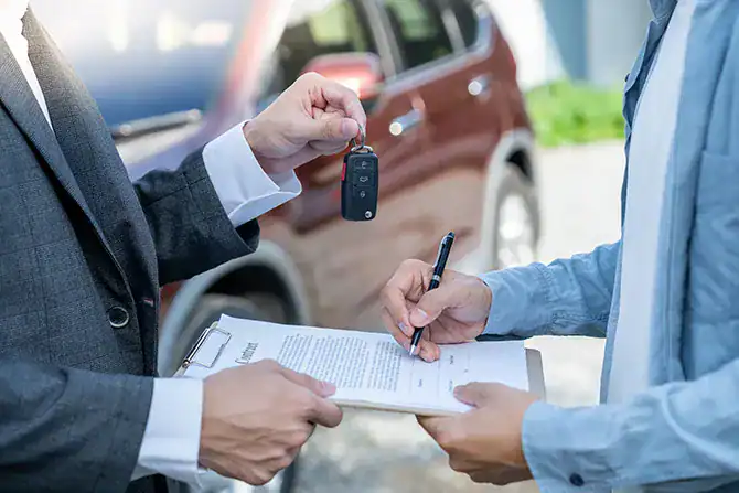 Customer signing paperwork while receiving car keys to a new, used, or leased car.