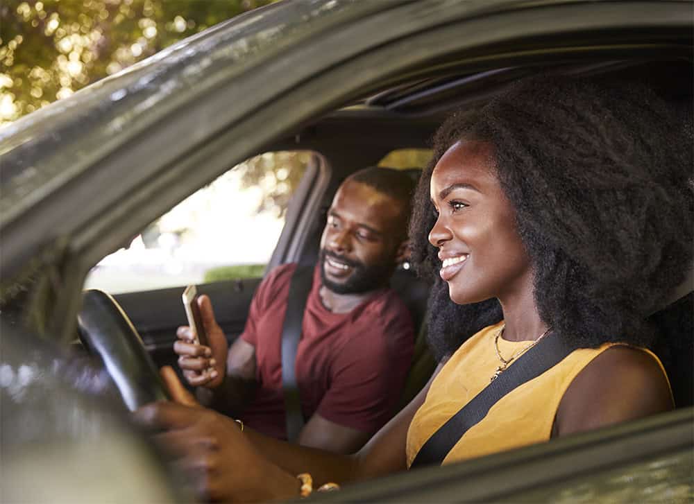 Two people enjoying a drive inside their new car, after completing their new auto loan.