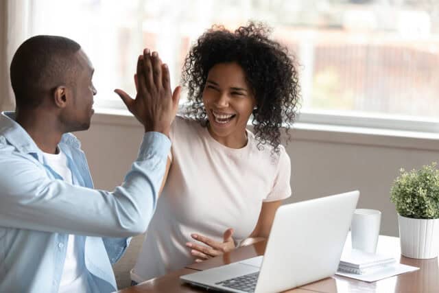 Two people collaborating and high-fiving in a bright office setting.
