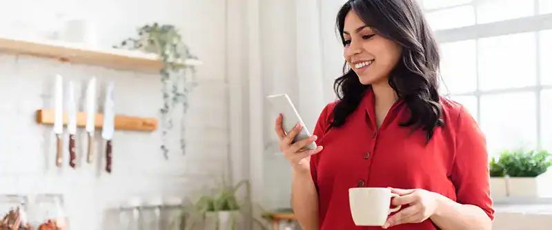 Happy woman in red shirt using smartphone to view digital services in her kitchen.