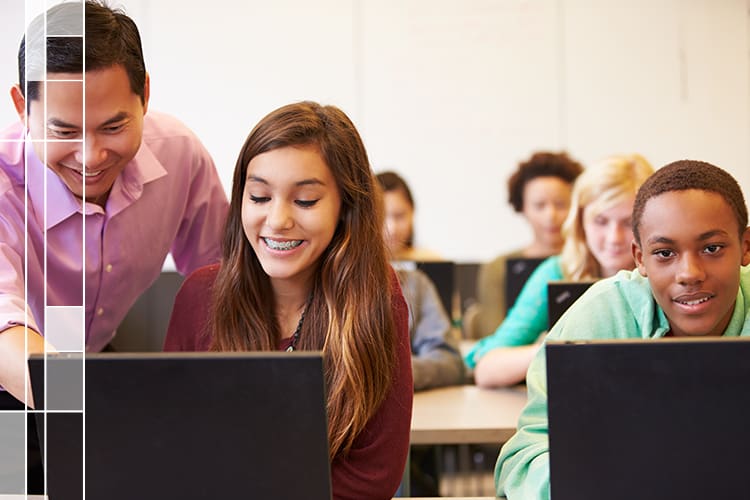 estudiantes trabajando en computadoras con un maestro ayudándolos