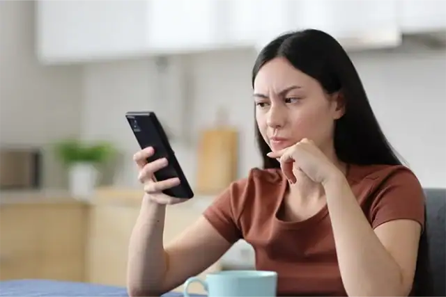 An image of a woman looking thoughtfully at her phone in a modern kitchen setting.