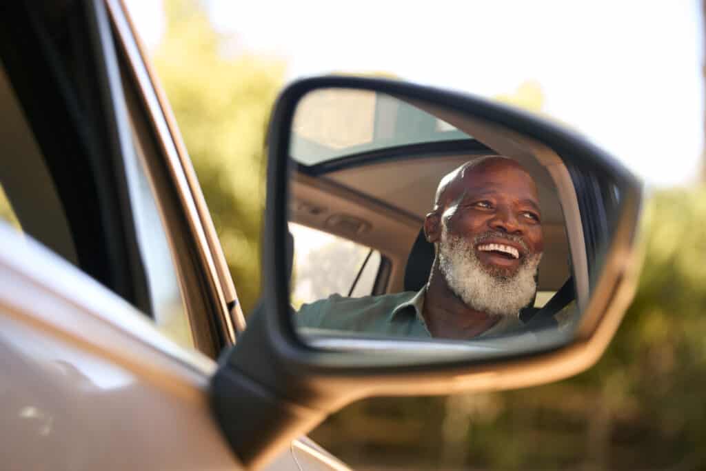 Older man in a car looking out the side mirror