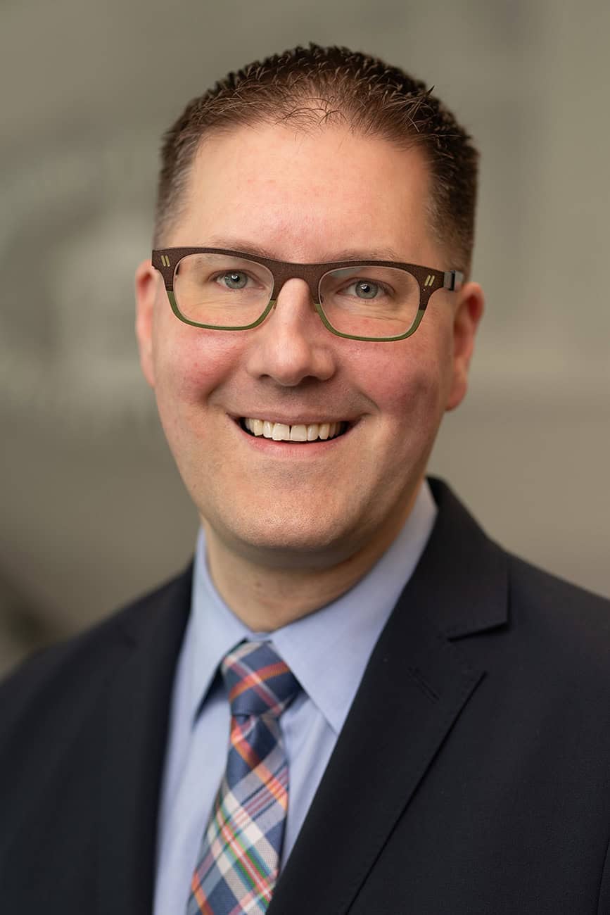 Professional headshot of a smiling man in a suit and glasses for Educators CU.
