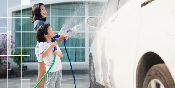 two kids washing a white car with hoses