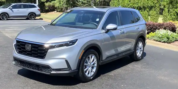 Silver Honda SUV parked in a lot with greenery in the background.