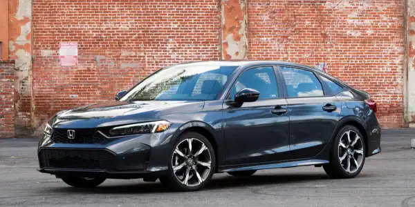 Black Honda Accord sedan parked on street in front of brick wall.