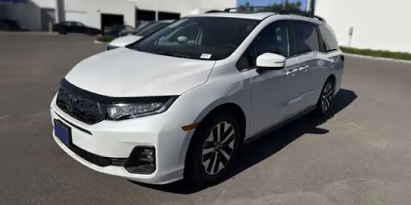 White Honda minivan parked in a lot with a modern building background.