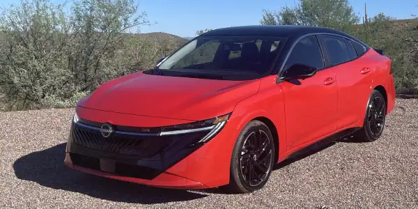 Red Nissan Sentra with black wheels parked in a natural setting.