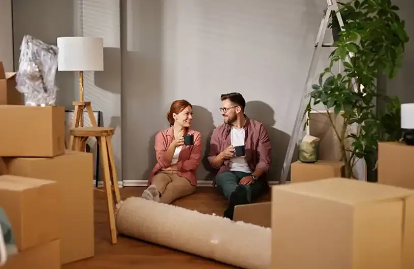 A first-time homebuyer couple enjoying coffee amid moving boxes and unpacked items.