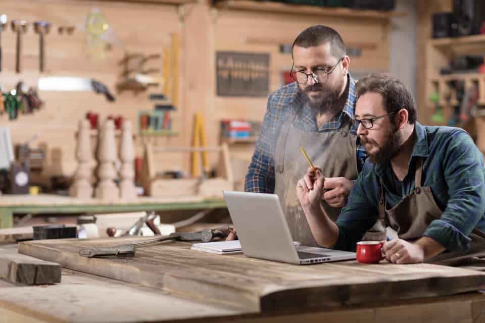 Two men in a workshop review notes on a computer