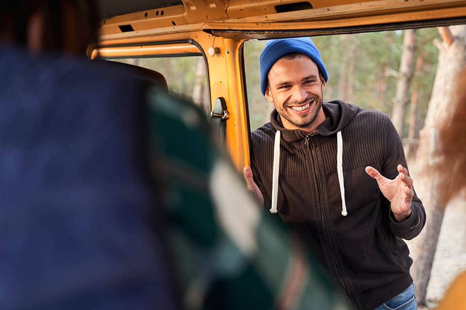 Man dressed in winter attire stands in a car doorway and smiles