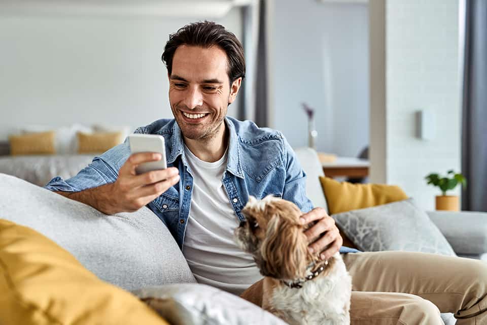 Hombre revisa su cuenta de ahorros en su teléfono mientras acaricia a su perro