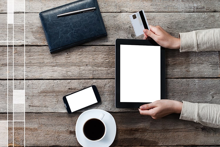 Monedero, café, celular y tableta en una mesa de madera con una mujer usando su tarjeta de crédito en la tableta