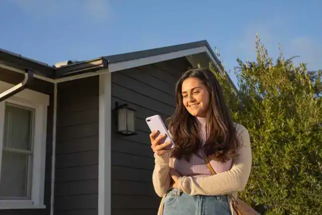 Zelle. Woman happily looking at her phone while standing outside.