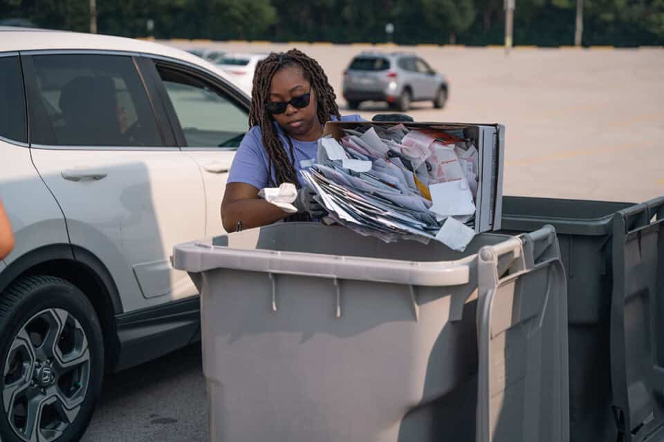 Woman disposing of papers into a trash bin for a shred day event.