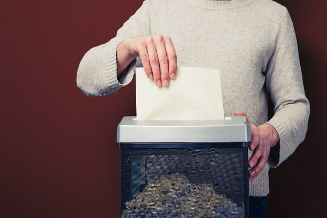 Individual shredding paper with a shredder in an office setting.