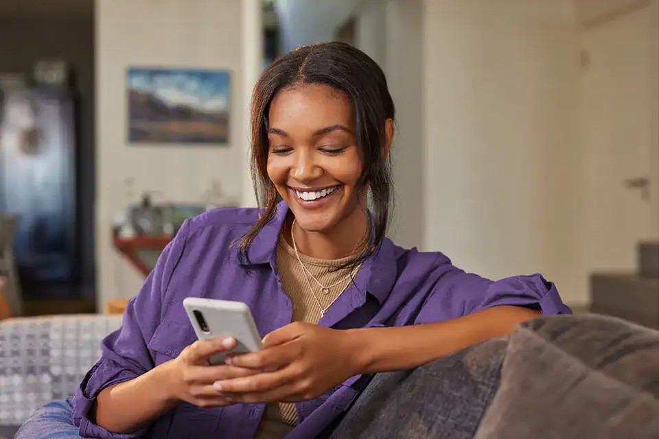 Happy woman using smartphone at home while receiving text messages for updates.