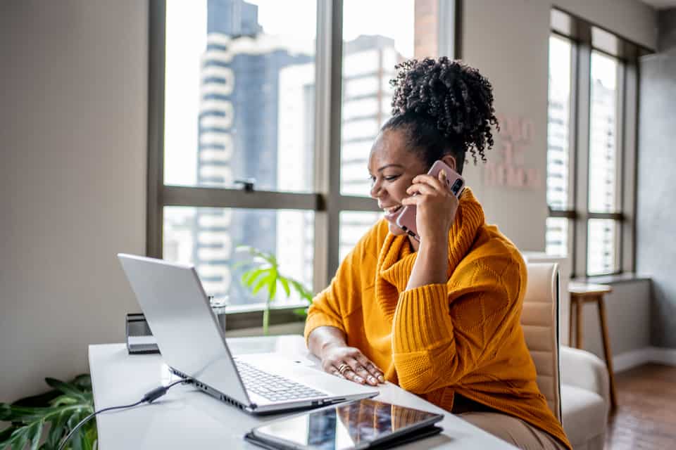 mujer sentada frente a su computadora mientras habla por teléfono