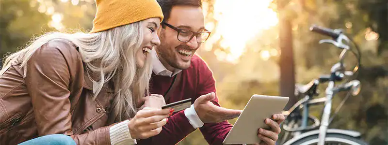 Happy couple using a tablet outdoors, representing their research into the benefits of a personal checking account.