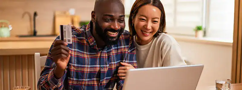 Happy diverse couple using a laptop at home to research what a checking account can do for them.