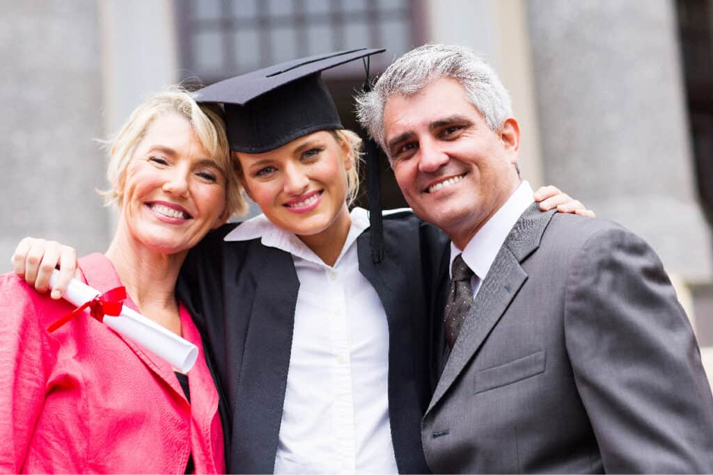 Teen in graduation cap smiling with parents.