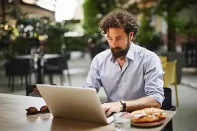 A man working on his laptop in a cafe outdoors.