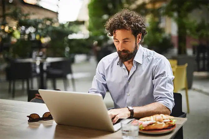 A man working on his laptop in a cafe outdoors.